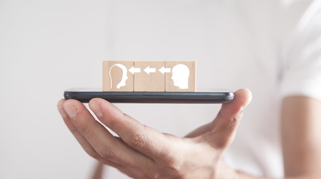 Homme tenant un smartphone avec un cubes en bois. Têtes humaines. Le transfert de connaissances
