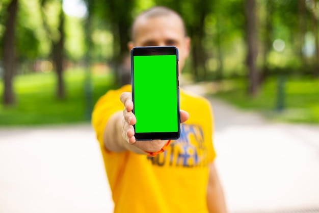 Homme tenant un smartphone avec écran chromakey vert Homme debout en plein air en journée d'été