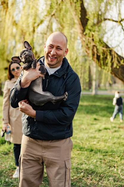 Homme tenant son chiot bouledogue français dans les mains tout en se promenant dans le parc