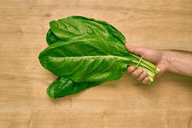 Homme tenant un tas d'épinards frais sur un comptoir de cuisine en bois.