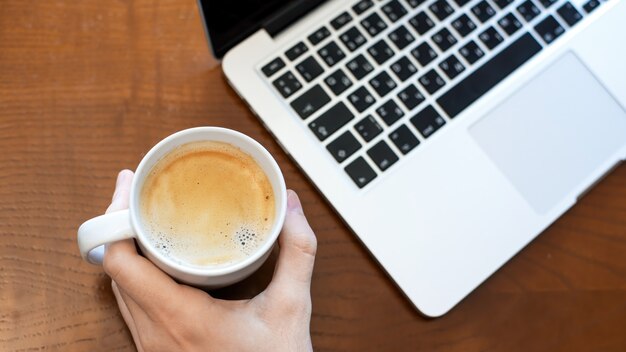 Un Homme Tenant Une Tasse De Café, Un Ordinateur Portable Sur La Table En Bois. Vue De Dessus