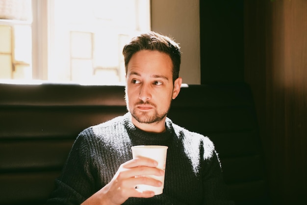 Photo homme tenant une tasse de café en papier à l'intérieur d'un café