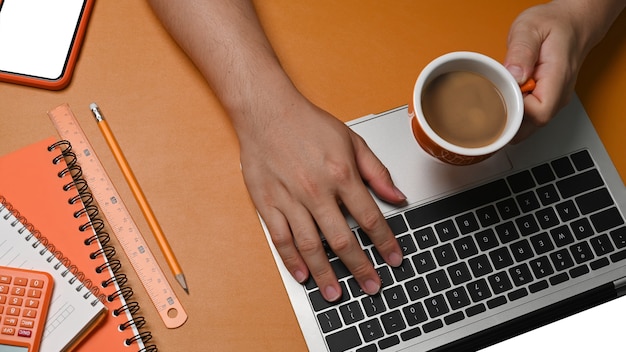 Photo homme tenant une tasse de café et utilisant un ordinateur portable sur du cuir marron.