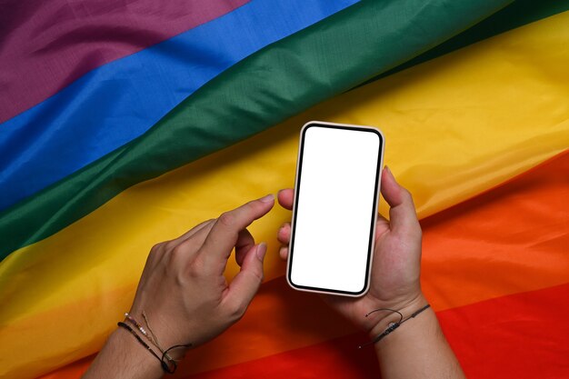 Homme tenant un téléphone intelligent avec un écran blanc sur un drapeau arc-en-ciel coloré. LGBT.