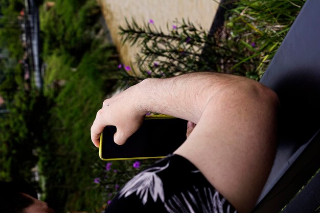 Photo un homme tenant un téléphone portable devant un mur avec des fleurs violettes.