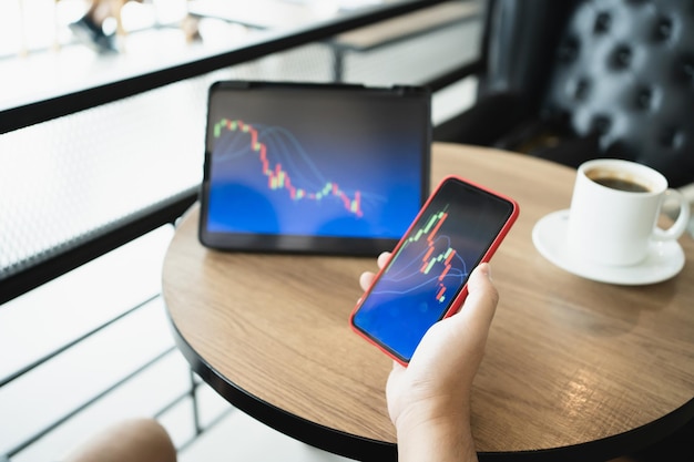 Homme tenant un téléphone et regardant un graphique en chandelier adapté au marché boursier forex ou cryptographie trading graphiques d'investissement financier Tendances de l'économie des finances Trading Stock Concept