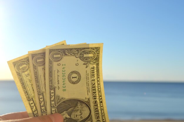 Un homme tenant trois billets d'un dollar dans sa main sur le fond de la mer bleue propre et du sk bleu