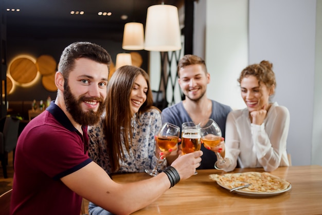 Homme tenant un verre de bière et assis dans une pizzeria avec des amis.