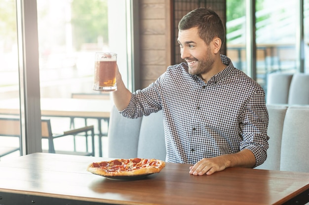 Homme tenant un verre de bière et regardant par la fenêtre du café