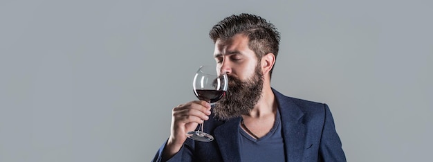 Homme tenant un verre de champagne à la main Homme avec un verre de vin rouge dans ses mains Homme barbu sommelier barbu dégustant du vin rouge