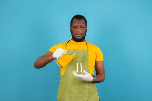 Un homme tenant un verre en versant du jus de fruit de la carafe se dresse sur le mur bleu.