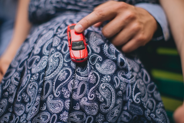 Homme tenant une voiture de jouet rouge sur le ventre de femme enceinte