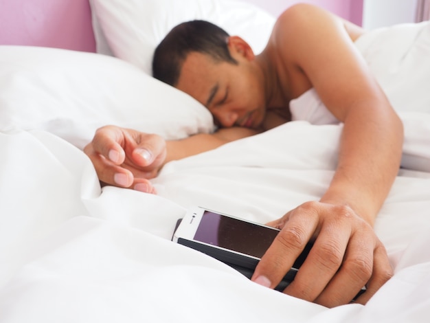 homme tenir mobile sur le lit et endormi