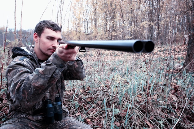 Homme en tenue de camouflage et avec un fusil de chasse dans une forêt lors d'une chasse au printemps