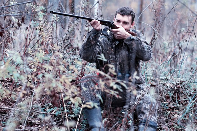 Photo homme en tenue de camouflage et avec un fusil de chasse dans une forêt lors d'une chasse au printemps