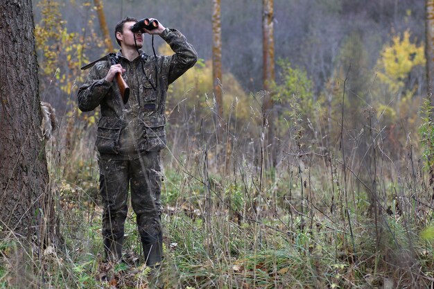 Un homme en tenue de camouflage et avec des fusils dans une ceinture forestière lors d'une chasse au printemps