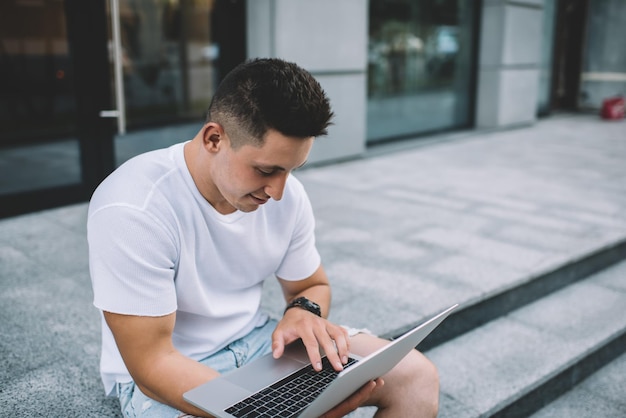 homme en tenue décontractée assis en milieu urbain et tapant le code du programme pendant le travail à distance millénaire