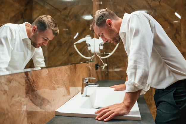 Un homme en tenue formelle est dans la salle de bain contre le miroir.