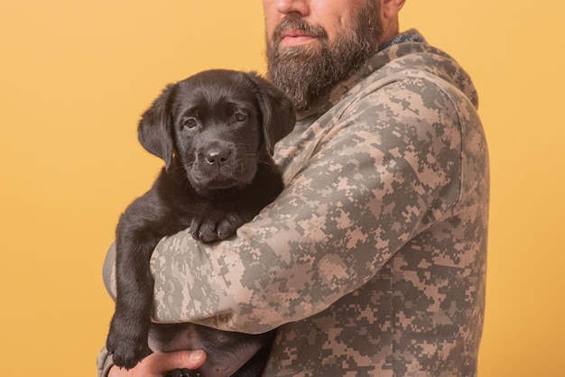 Homme en tenue militaire avec un chiot Labrador Retriever dans ses bras