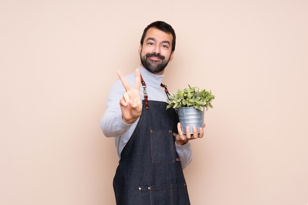 Homme, tenue, plante, mur isolé, sourire, projection, signe victoire