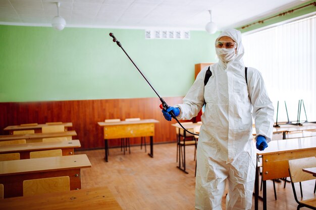 Homme en tenue de protection désinfectant une salle de classe