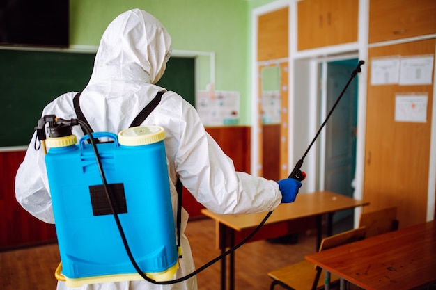 Homme en tenue de protection désinfectant une salle de classe