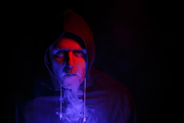 Un homme en tenue de protection exhale de la fumée. Concept d'image d'Halloween. Protection antivirus. Illuminé avec des lumières colorées