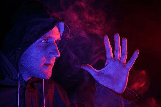 Un homme en tenue de protection exhale de la fumée. Concept d'image d'Halloween. Protection antivirus. Illuminé avec des lumières colorées