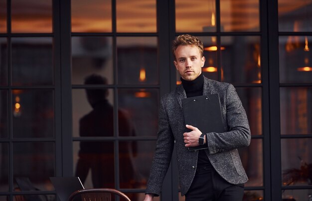 Homme en tenue de soirée élégante à l'extérieur contre un bâtiment moderne.