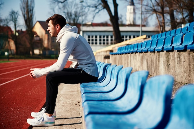 Homme en tenue de sport se reposant au siège du stade après des exercices