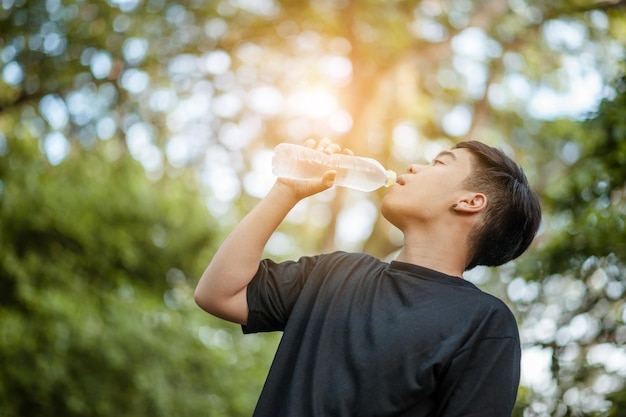 Homme thaïlandais buvant de l'eau les yeux fermés après des exercicesBouteille d'eau en plastique après l'entraînement à l'extérieurPortrait extérieur d'un beau jeune homme buvant de l'eau sur le courtxA