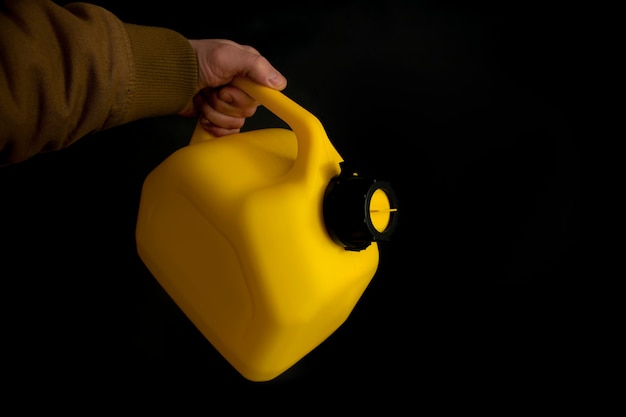 L'homme tient un bidon en plastique jaune pour le carburant de voiture dans sa main sur un fond noir. Maquette d'un conteneur pour liquides et carburants dangereux.