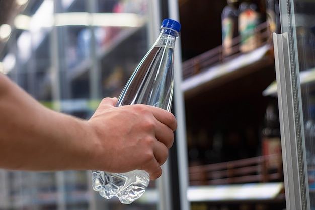 L'homme tient dans sa main une bouteille en plastique avec de l'eau minérale pure sur le fond d'une vitrine.