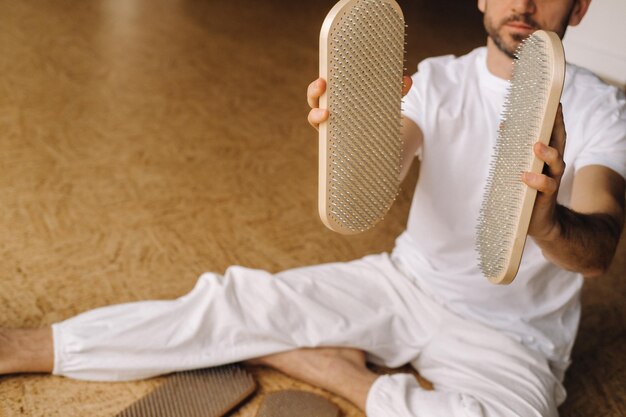 Un homme tient dans ses mains des planches avec des clous pour les cours de yoga