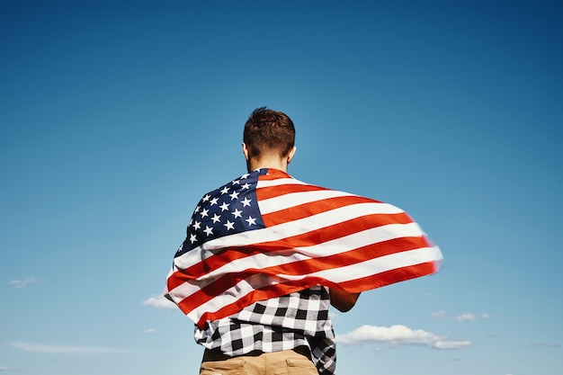 L'homme tient le drapeau national des Etats-Unis contre le ciel nuageux bleu