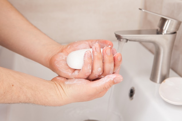 Un homme tient du savon dans ses mains au-dessus du lavabo.