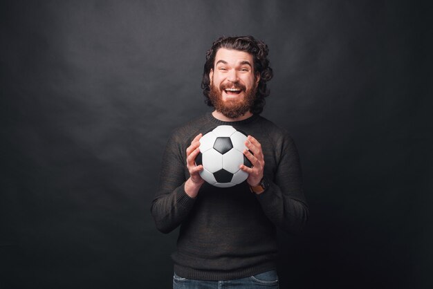 Un homme tient excité un ballon de football près d'un mur noir