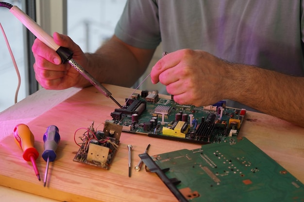 Un homme tient un fer à souder dans sa main et soude un microcircuit