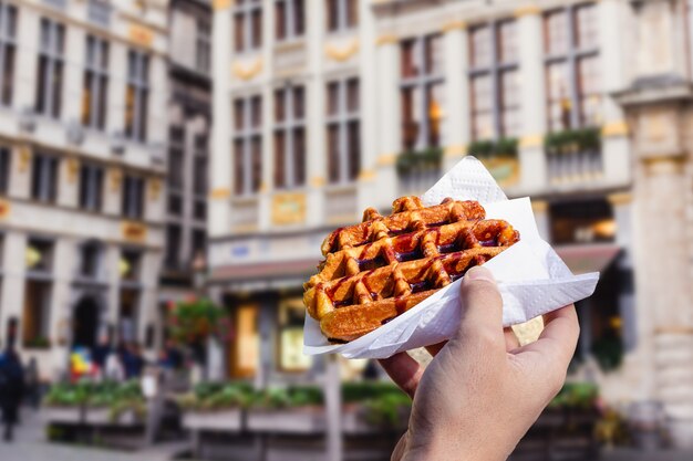 L'homme tient la gaufre avec une sauce au chocolat sur le fond de la ville