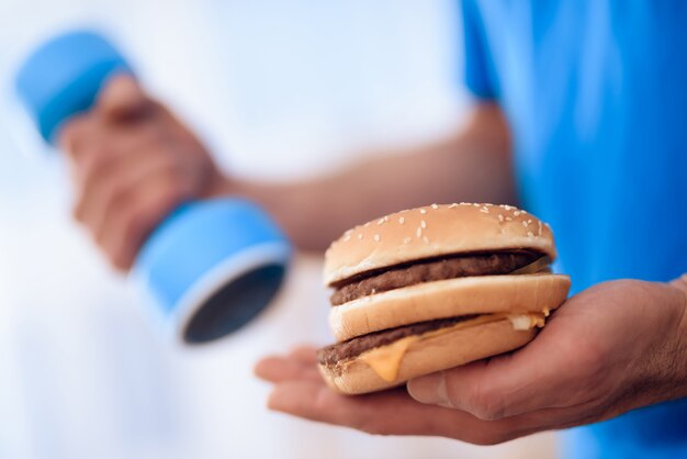 Un homme tient un hamburger dans une main, dans un autre haltère.