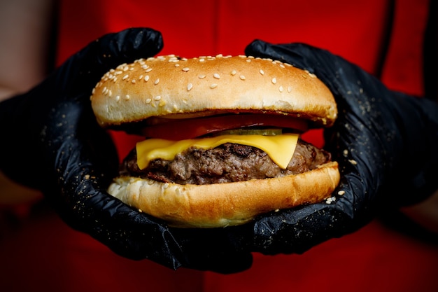 L'homme tient un hamburger savoureux prêt dans les mains dans des gants noirs.