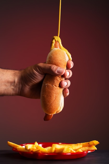 Un homme tient un hot-dog avec sa main. La moutarde s'égoutte sur un hot-dog, fond rouge