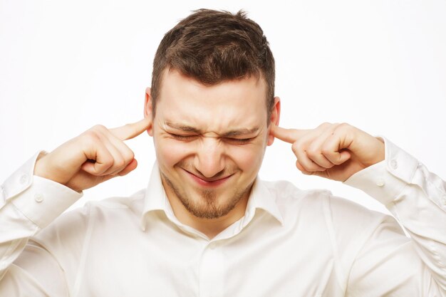 L'homme tient les mains sur les oreilles des temples, le concept d'homme stressé, mal de tête, déprimé, douleur, les yeux fermés portent un t-shirt blanc, isolé sur blanc.