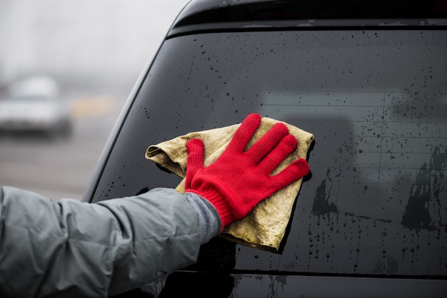 L'homme tient la microfibre à la main et polit la voiture en verre.