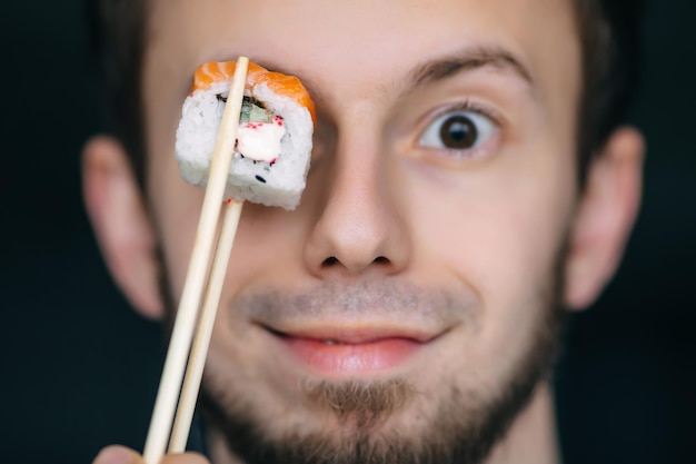 L'homme tient un morceau de rouleau de sushi devant ses yeux