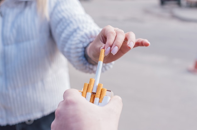 Un homme tient un paquet de cigarettes dans ses mains et donne une cigarette à une fille.
