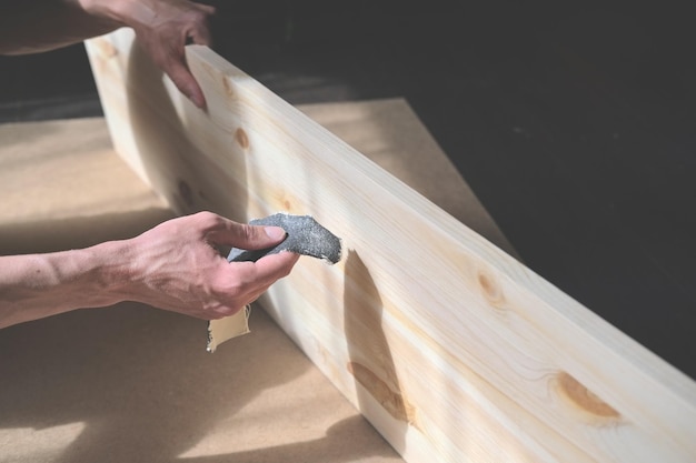 L'homme tient une planche de bois avec ses mains et polir le bord avec du papier de verre pour faire des meubles faits à la main