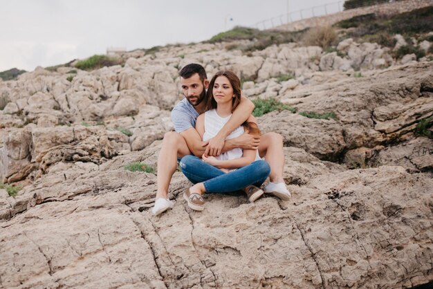 Un homme tient sa petite amie alors qu'ils sont tous les deux assis sur les rochers en Espagne