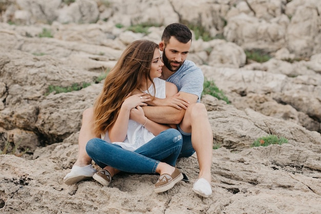 Un homme tient sa petite amie alors qu'ils sont tous les deux assis sur les rochers en Espagne