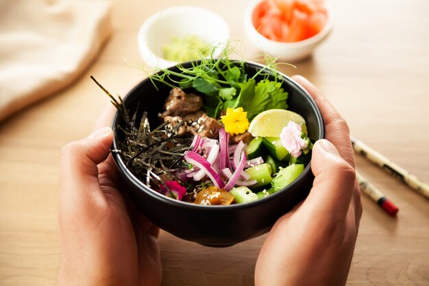 un homme tient une salade poke avec du boeuf dans un bol dans ses mains ingrédients boeuf nameko champignons cerise